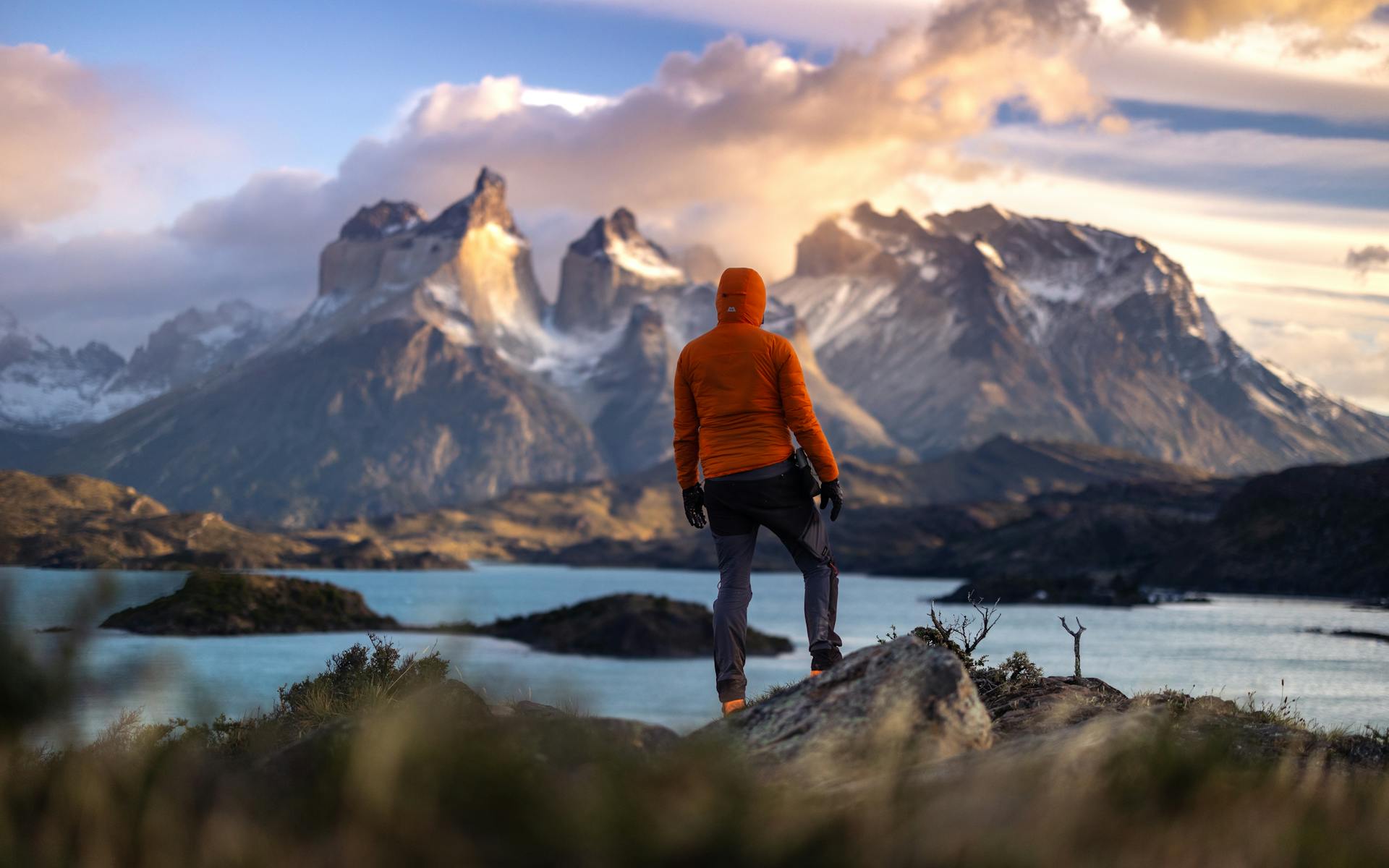 Person in orange jacket facing dramatic mountain peaks and turquoise lake